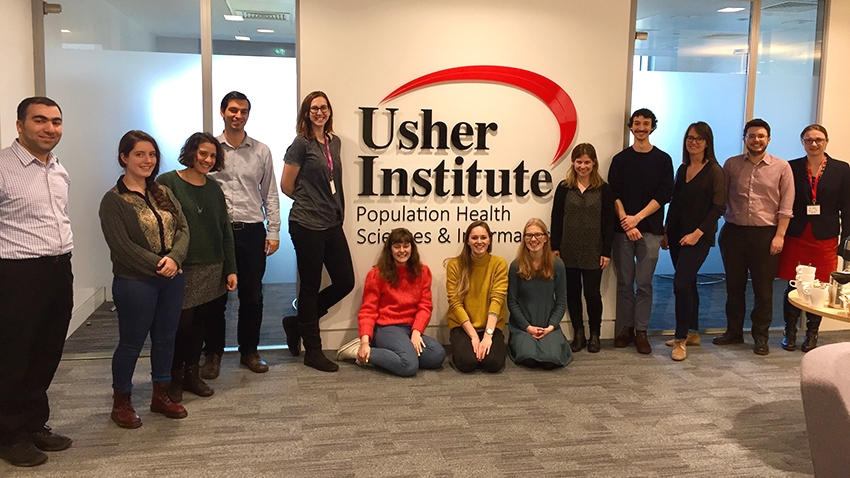 Attendees of the workshop stand for a group picture in front of the Usher Institute logo